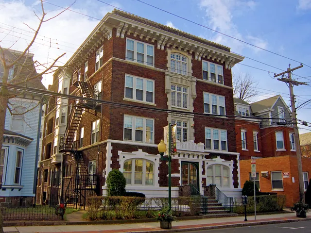 The four-storey red brick apartment building at 1214 Chapel Street, its white-trimmed bay windows and arched entrance above a low hedge, a Chapel West banner on the lamppost out front