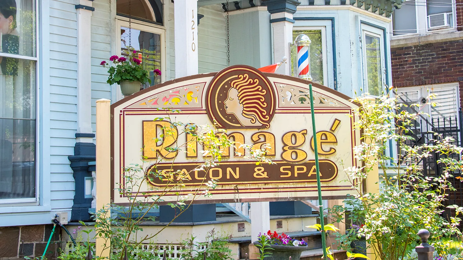 Rimage Salon and Spa's painted hanging sign in front of a pale Victorian house, a barber pole beside the door